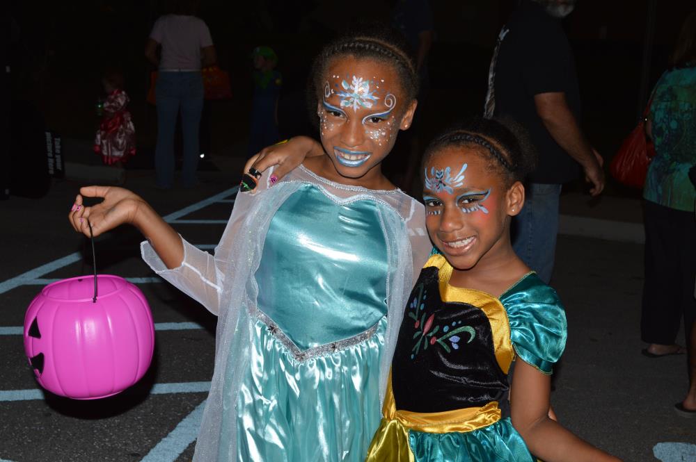 Two girls dressed as princesses, one holding plastic, pink jack-o-lantern